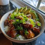A delicious Teriyaki Chicken Avocado Rice bowl topped with sesame seeds and green onions.