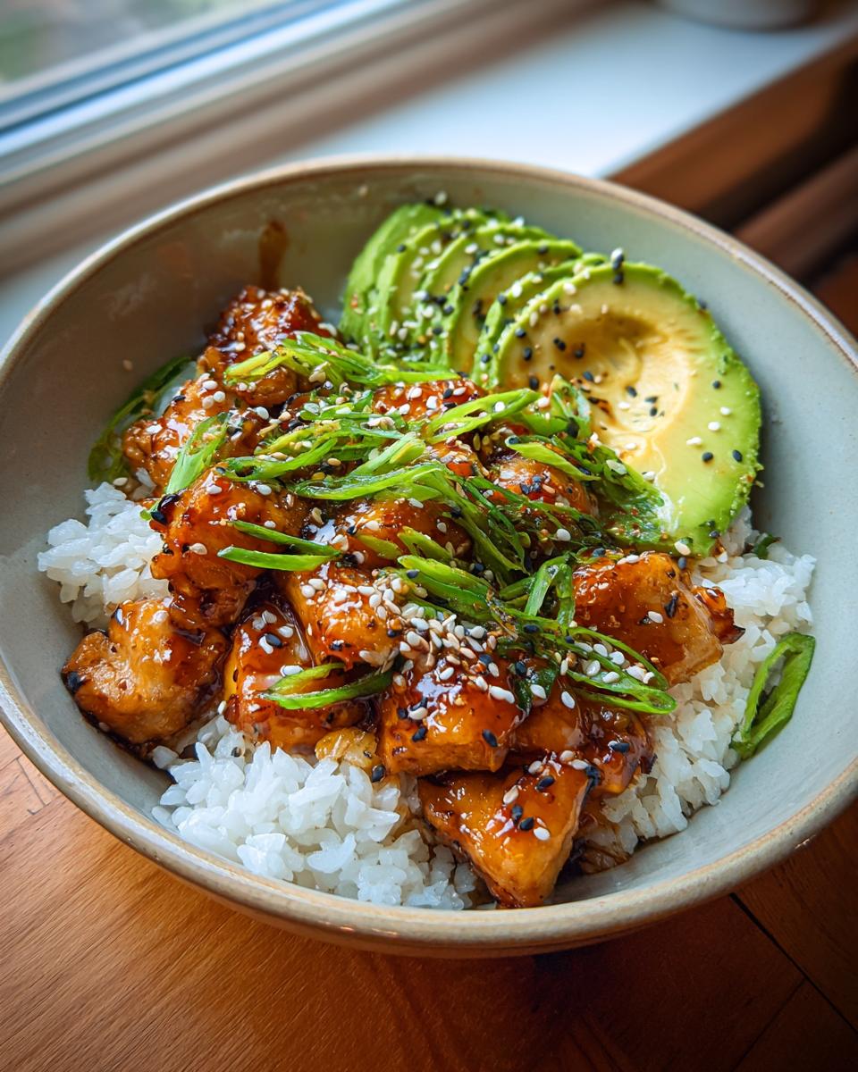 A delicious bowl of Teriyaki Chicken Avocado Rice, garnished with sesame seeds and green onions.