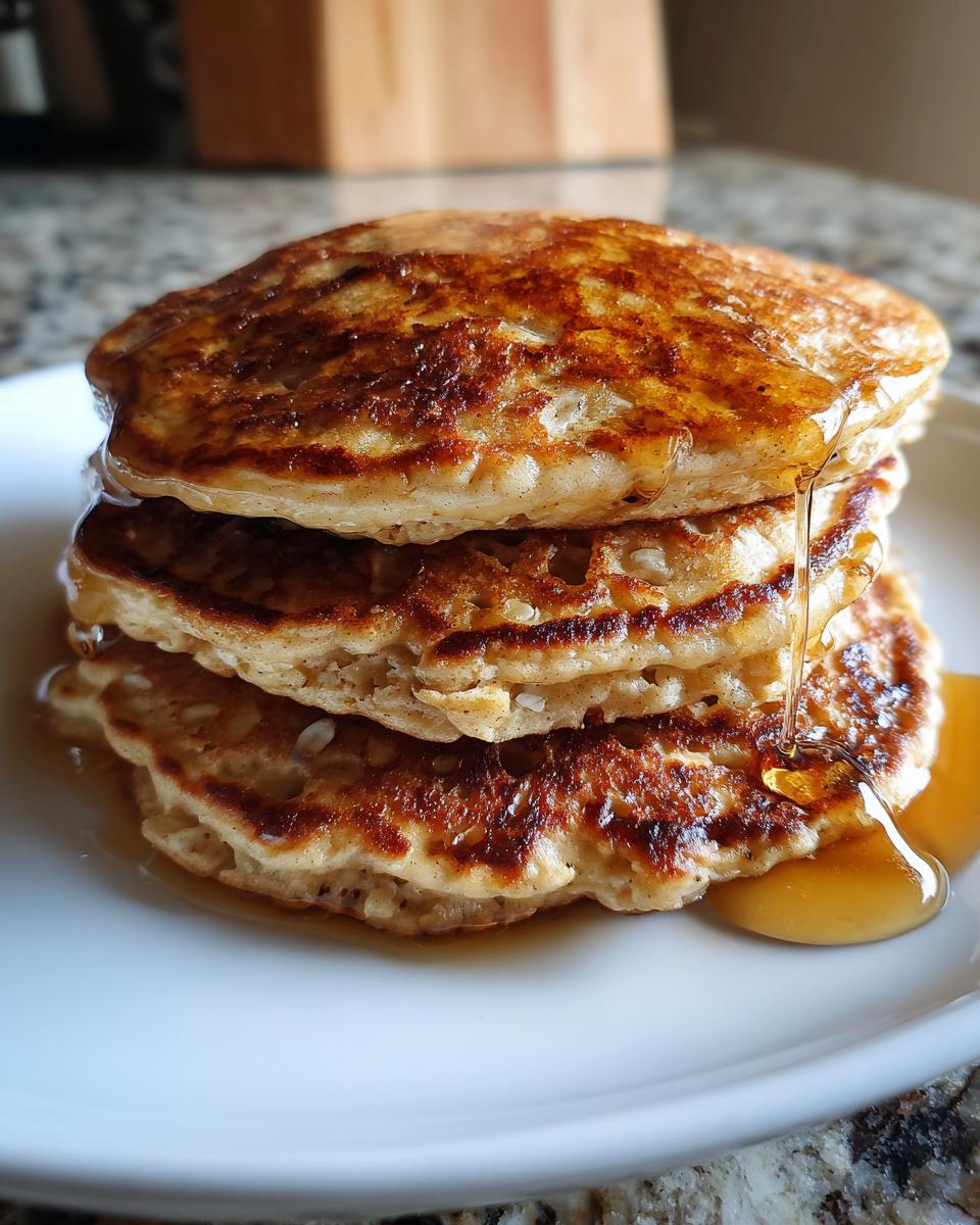 A stack of three Banana Oat Pancakes on a white plate, drizzled with syrup.