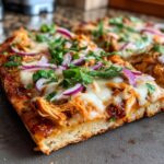 Close-up of a slice of BBQ Chicken Flatbread topped with red onion and cilantro.