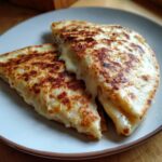 Two golden-brown Beef and Cheese Quesadillas with melted cheese oozing out on a plate.