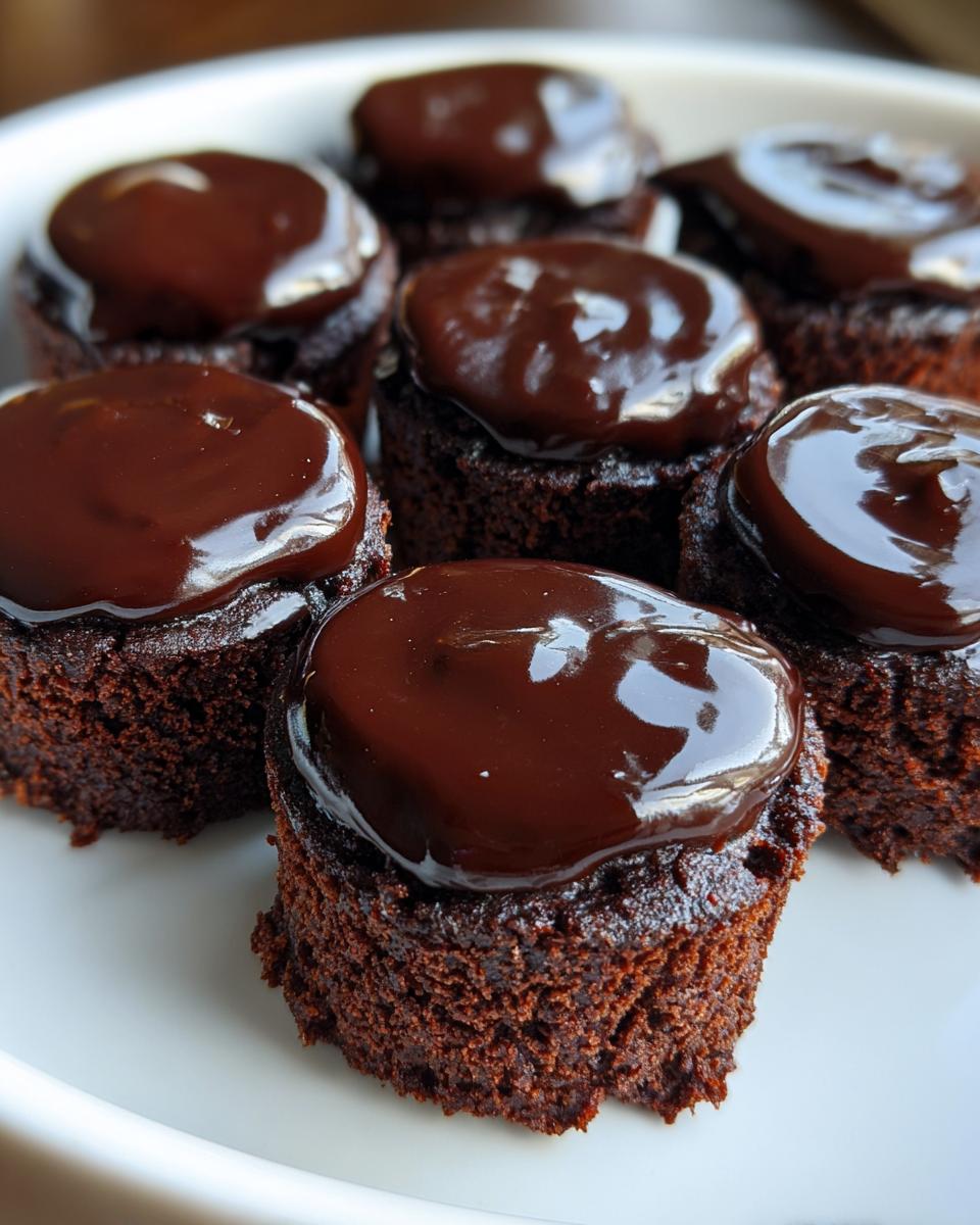 Several homemade Brownie Bites with Ganache topping, arranged on a white plate.