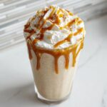 A tall glass filled with a homemade Caramel Frappuccino Copycat, topped with whipped cream and caramel drizzle.