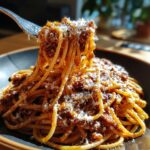 A fork lifting a portion of Classic Spaghetti with Meat Sauce, topped with grated cheese, from a bowl.