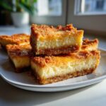 A stack of Easy Cheesecake Bars with a crumbly topping on a white plate, showcasing the creamy filling.