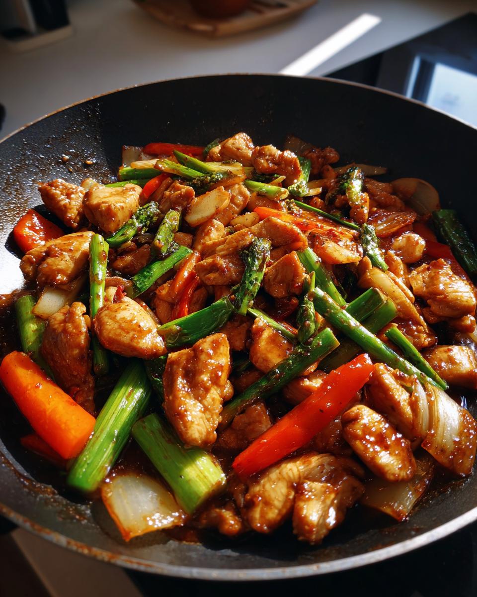 Close-up of Easy Chicken Stir Fry with Veggies in a pan, featuring chicken, asparagus, carrots, and onions.