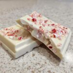 Two pieces of Easy Christmas Candy Bark, featuring white chocolate and crushed peppermint candies.