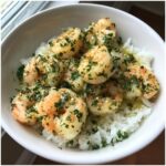 Overhead shot of a Garlic Butter Shrimp Rice Bowl in a white bowl, garnished with fresh herbs.