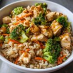 A bowl of Healthy Chicken Rice Bowls with broccoli, carrots, and a savory sauce.