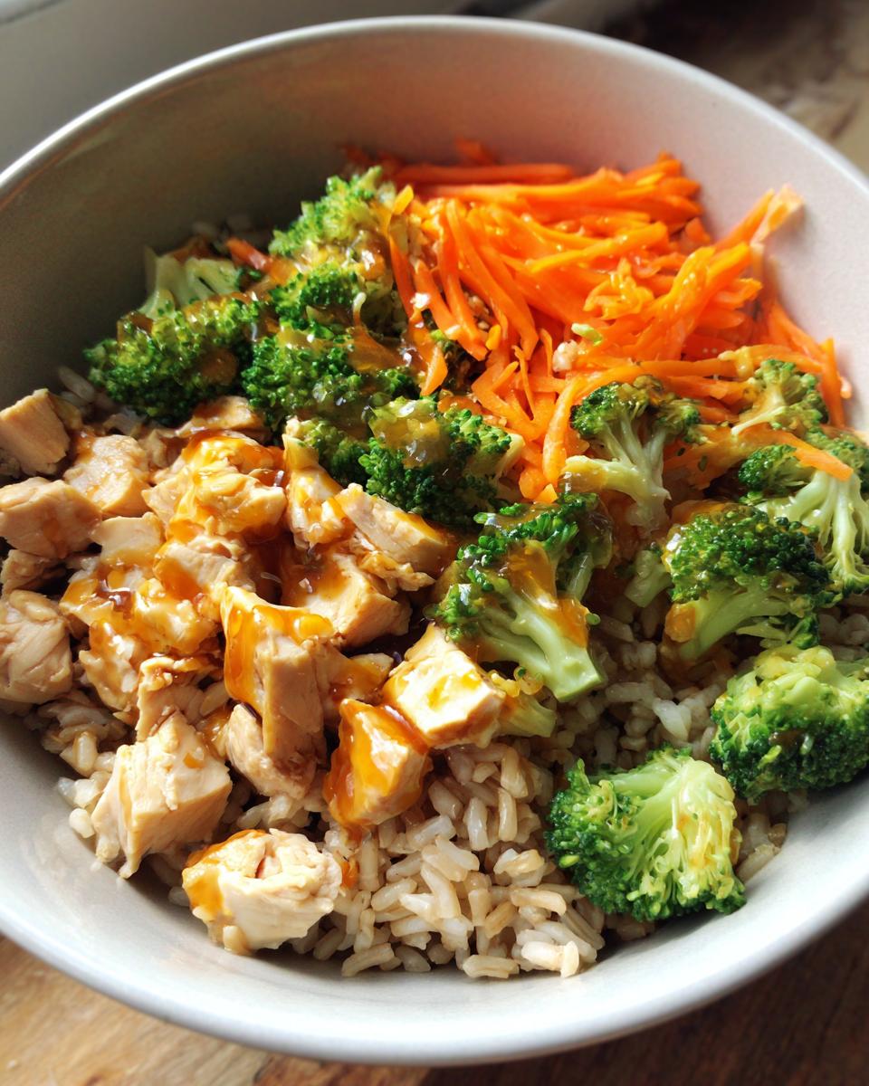 A vibrant bowl of Healthy Chicken Rice Bowls featuring chicken, brown rice, broccoli, carrots, and a savory sauce.