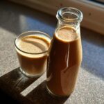 A glass and bottle filled with homemade Baileys, showcasing its creamy texture and rich color.