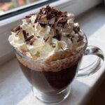 A glass mug filled with Hot Chocolate Starbucks Style, topped with whipped cream and chocolate shavings.