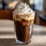 A refreshing Iced White Mocha Recipe in a clear glass, topped with whipped cream.