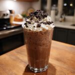 A tall glass of Mocha Cookie Crumble Frappuccino topped with whipped cream and cookie crumbles.