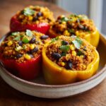 Red and yellow Quinoa Stuffed Bell Peppers filled with quinoa, black beans, and corn, garnished with cilantro.