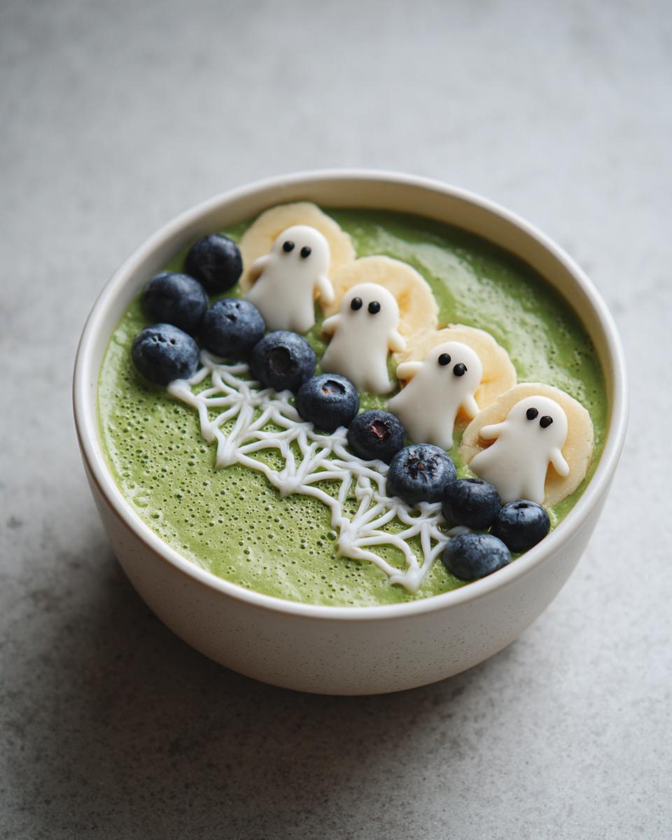 A Spooky Halloween Smoothie Bowl decorated with ghost-shaped candies, blueberries, banana slices, and a spiderweb design.