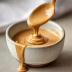 A spoonful of Sweet Irish Cream Dessert Sauce being poured into a bowl, creating a swirl.