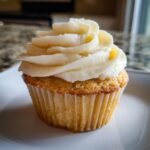 A single vanilla cupcake with buttercream frosting on a white plate, ready to eat.