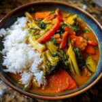 A vibrant Vegetable Curry Bowl with rice, featuring broccoli, carrots, peppers, and zucchini in a rich curry sauce.