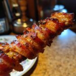 Close-up of a perfectly cooked Bacon-Wrapped Date on a stick, showcasing crispy bacon and a hint of sweetness.