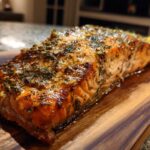 Close-up of a flaky, golden-brown baked salmon fillet seasoned with fresh dill and lemon.