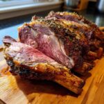 Close-up of a perfectly cooked BEST Prime Rib roast, sliced to reveal a juicy pink interior and herb crust.