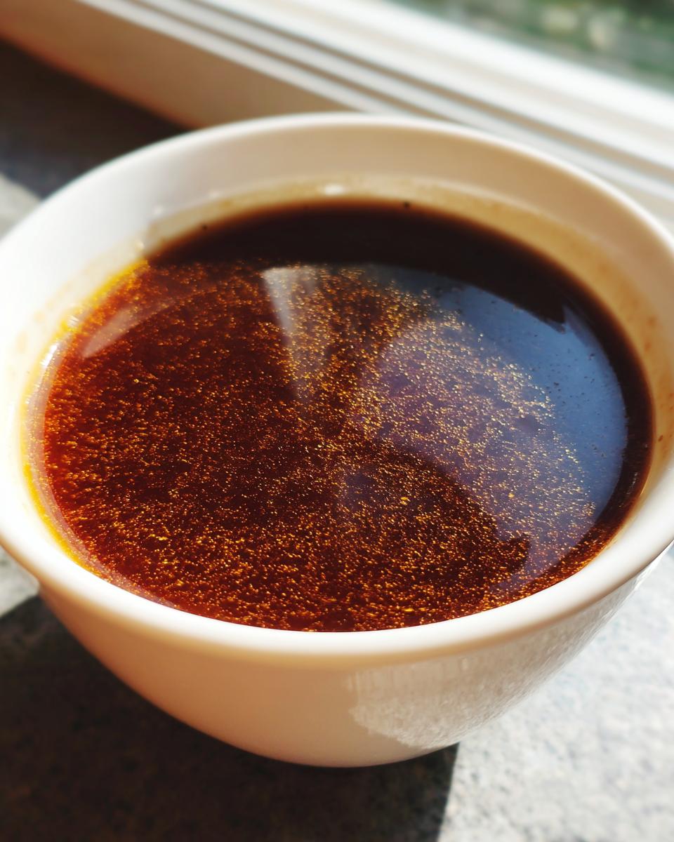 A close-up of rich, dark The Classic Au Jus: Unbeatable Flavor Every Time in a white ramekin, with shimmering oil droplets.