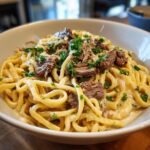 A close-up of a bowl of creamy Prime Rib Pasta topped with shredded beef and fresh parsley.
