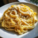 A close-up of a white bowl filled with creamy truffle pasta, topped with grated parmesan and cracked black pepper.