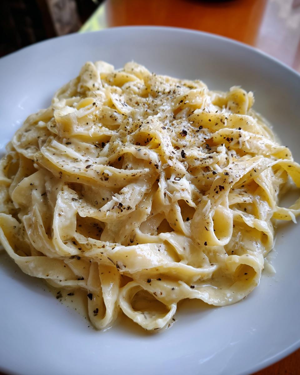 Close-up of a bowl of Creamy Truffle Pasta, garnished with black pepper and grated cheese.