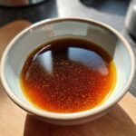 A close-up of a small bowl filled with rich, dark homemade Au Jus, perfect for beef dishes.