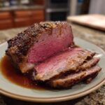 A perfectly cooked, juicy prime rib roast, sliced and served with rich au jus on a plate.