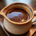 Close-up of a rich, dark au jus in a ceramic gravy boat, perfect for dipping.
