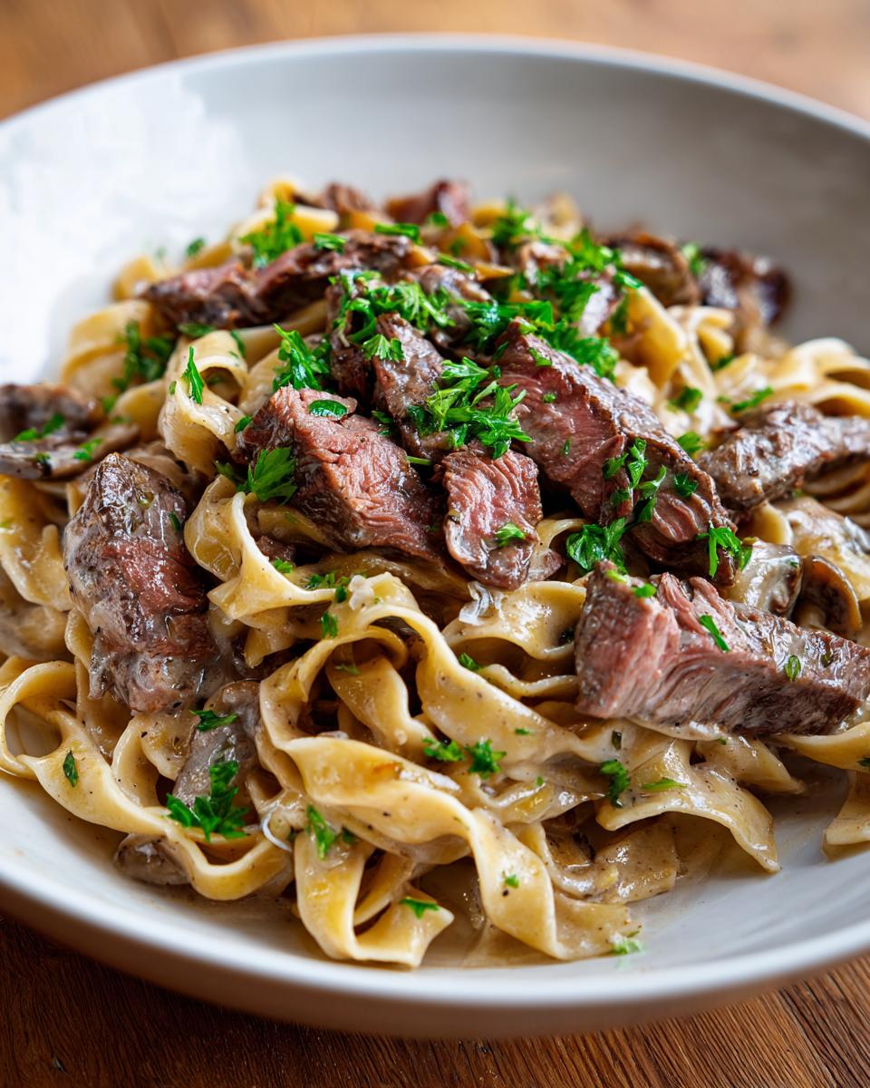 A close-up of creamy Prime Rib Pasta topped with tender slices of seared steak and fresh parsley.