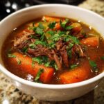 A close-up of a bowl of Prime Rib Soup, featuring tender shredded beef, chunks of carrots, and fresh parsley garnish.