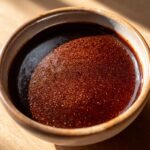 A close-up of a bowl filled with rich, dark, and velvety au jus, showcasing its glossy texture and fine bubbles.