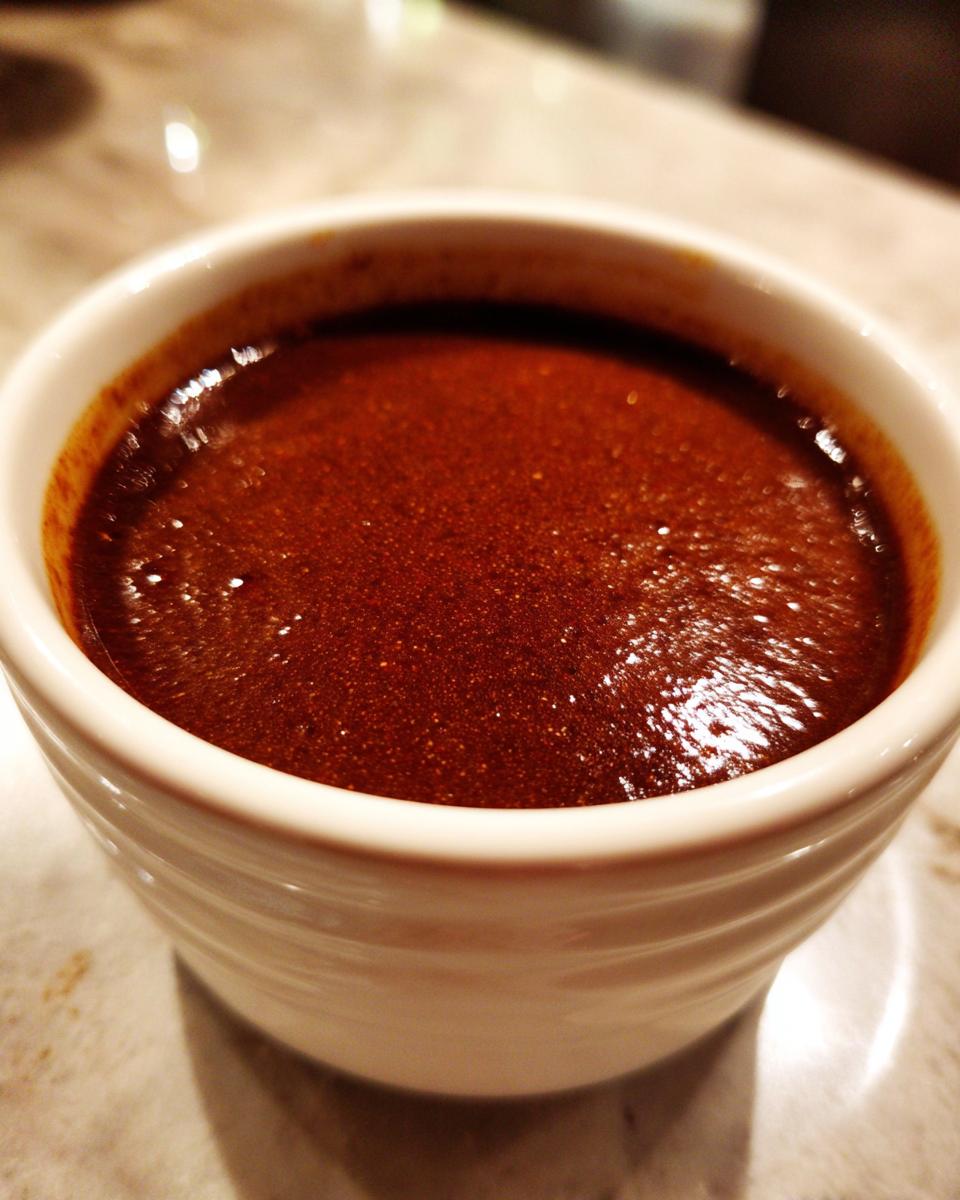 A close-up of a white ramekin filled with rich, dark, velvety au jus.