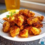 A close-up of golden brown, seasoned Air Fryer Chicken Bites piled high on a white plate.