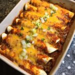 Close-up of baked Beef Enchiladas covered in melted cheddar cheese and topped with chopped green onions.