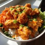 Close-up of a delicious Bang Bang Chicken Bowl featuring crispy fried chicken pieces drizzled with orange sauce over rice and lettuce.