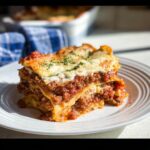 A thick, layered slice of rich Beef Lasagna with meat sauce and melted cheese on a white plate.