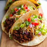 Two soft shell tacos filled with seasoned ground beef, lettuce, cheese, diced tomatoes, and red onion, perfect for Best Ground Beef Tacos.