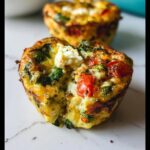 Close-up of a single Breakfast Meal Prep Egg Cup, showing eggs, spinach, tomato, and feta cheese filling.