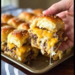 A hand pulling apart a cheesy Cheeseburger Sliders Bake, showing melted cheese dripping.
