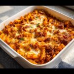 Close-up of a golden-brown Budget Pasta Bake topped with melted, bubbly cheese in a white baking dish.