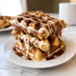 A tall stack of three Cinnamon Roll Waffles generously drizzled with white icing and brown cinnamon glaze.