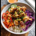 Close-up of a vibrant Bang Bang Chicken Bowl featuring crispy chicken, rice, red cabbage, carrots, and drizzled with orange sauce.