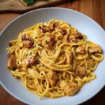 A close-up of a white bowl filled with Cowboy Butter Chicken Linguine, featuring creamy sauce and seared chicken pieces.