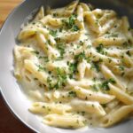 A close-up, top-down view of a bowl filled with rich Creamy Garlic Penne pasta, topped with fresh chopped parsley.