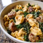 Close-up of Creamy Sausage Tortellini Skillet with kale in a white bowl, coated in a rich sauce.